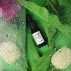 Close-up shot of a clear glass bottle of face serum with dropper, styled with natural leaves and soft lighting, captured by Emipix Solutions photography studio in Jaipur.